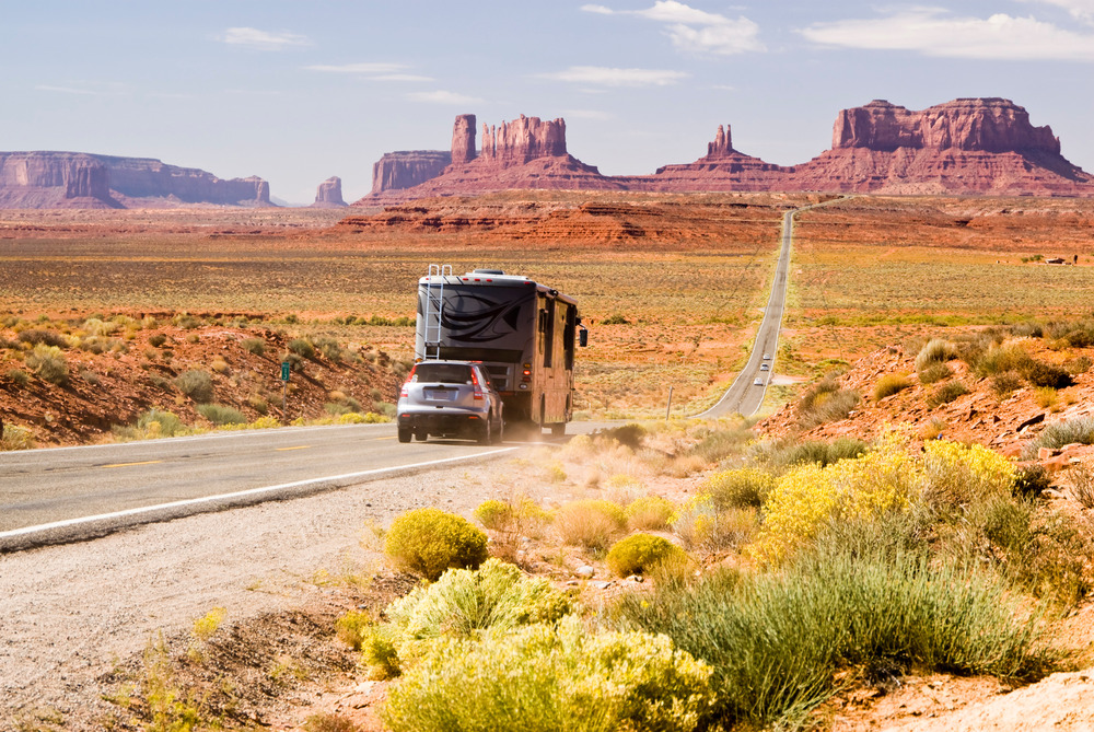 RV driving through Monument Valley towing a car